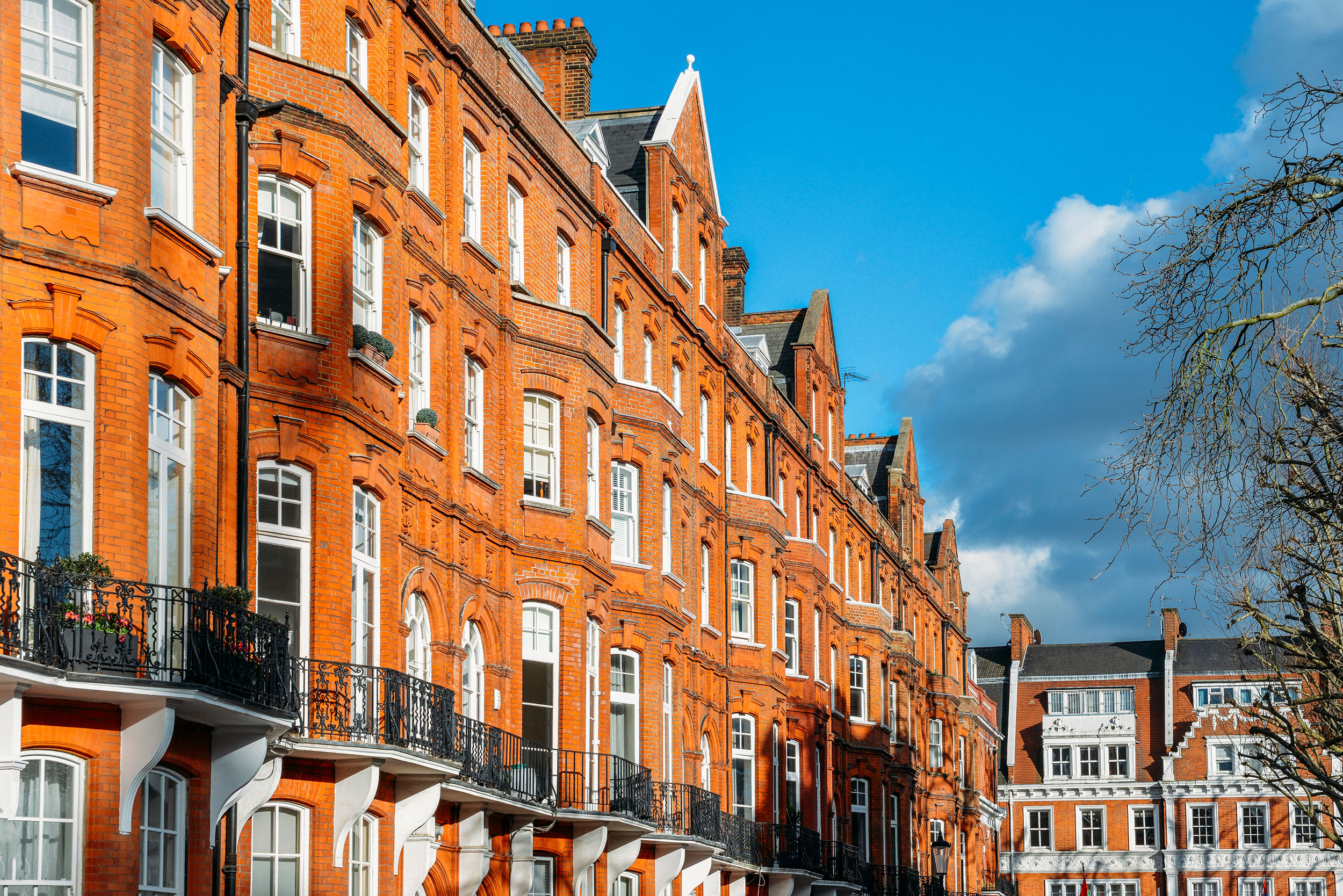 Row of red-brick period apartment buildings with iron balconies under a blue sky